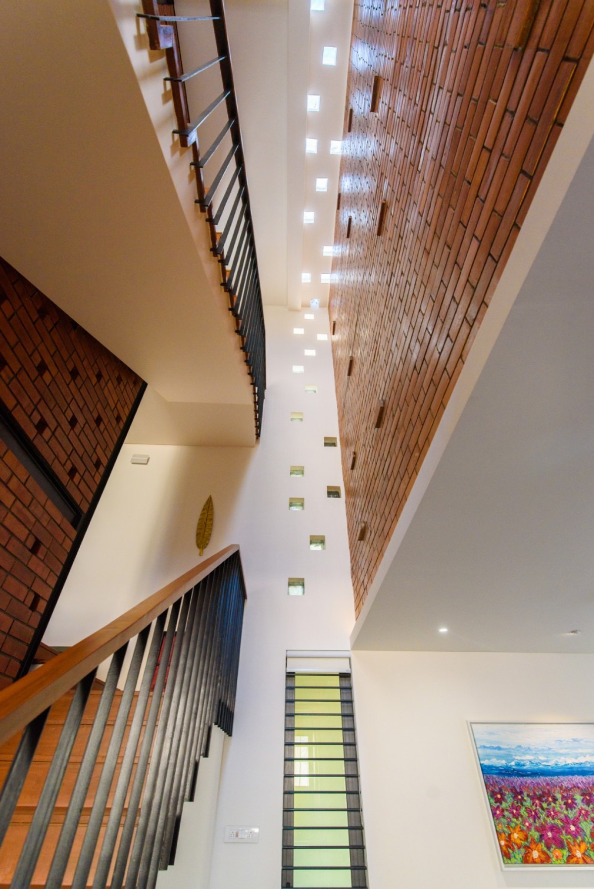 Staircase triple height void dressed in glass blocksy on wall &  roof of Corner Brick House by Jacob + Rathodi Architects