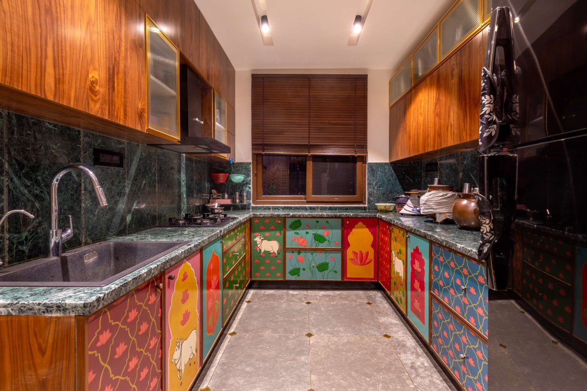 A colourful surprise, the Pichwai themed kitchen features hand-painted shutters on the lower cabinets. – Kuteeram by Brick and Compass