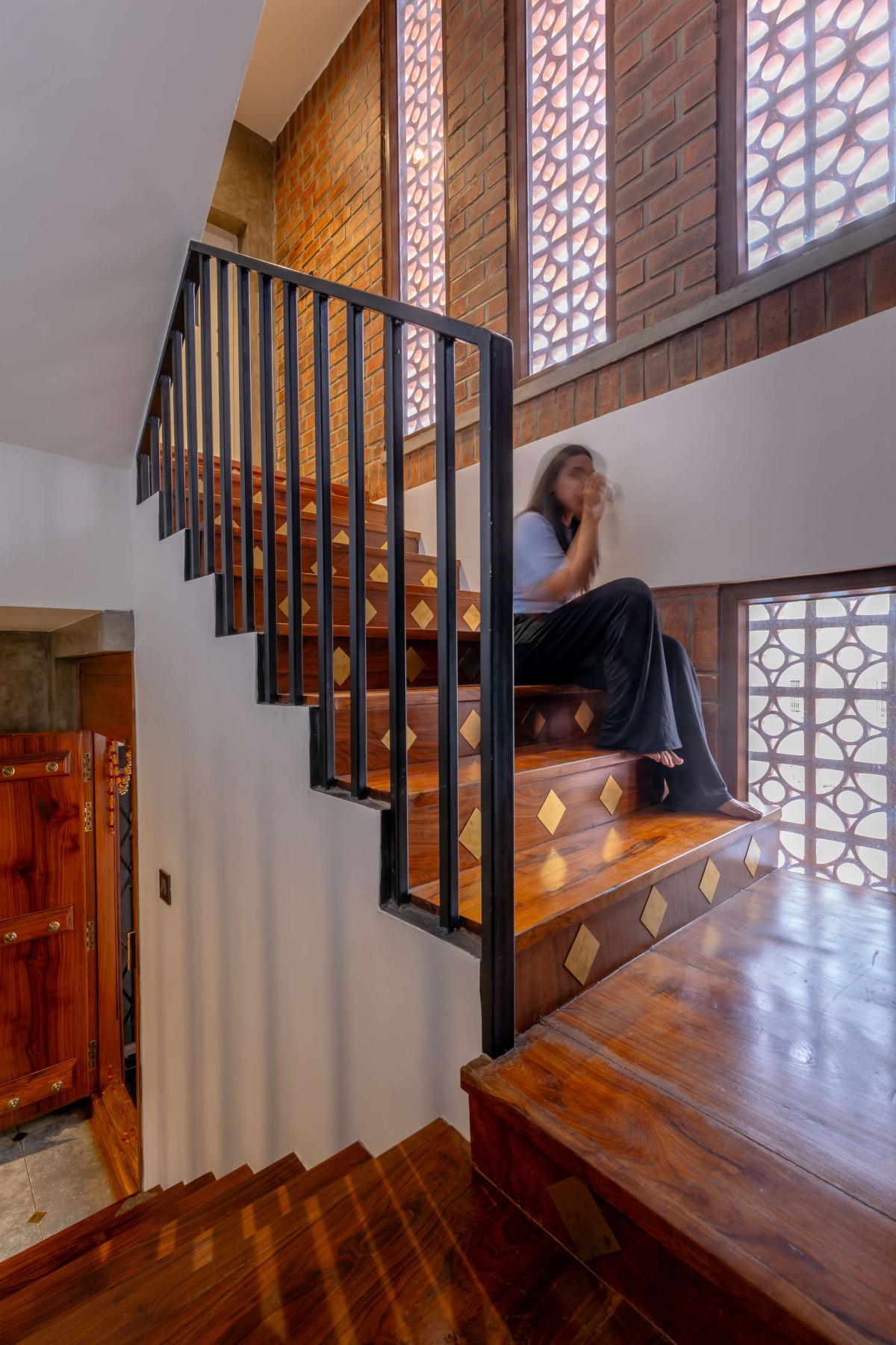 Wooden staircase adorned with sparkling brass motifs, Long vertical windows with Terracotta Jaali bring setting the character – Kuteeram by Brick and Compass
